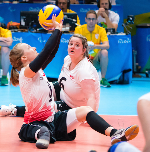 Jolan setting the volleyball from a seated position. She is wearing a white team Canada jersey