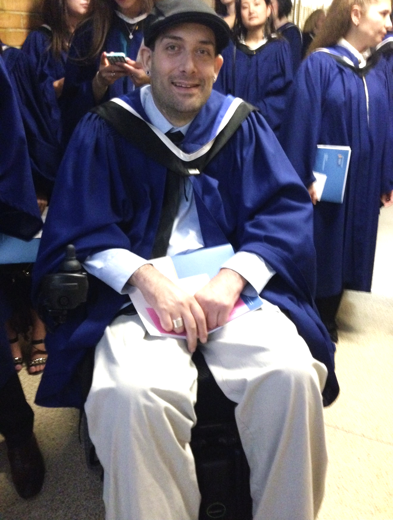 Man in a wheelchair holding a carpet and wearing graduation attire