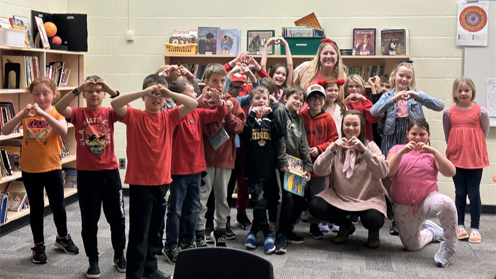 A group of grade three students smiling and making heart shapes with their hands,