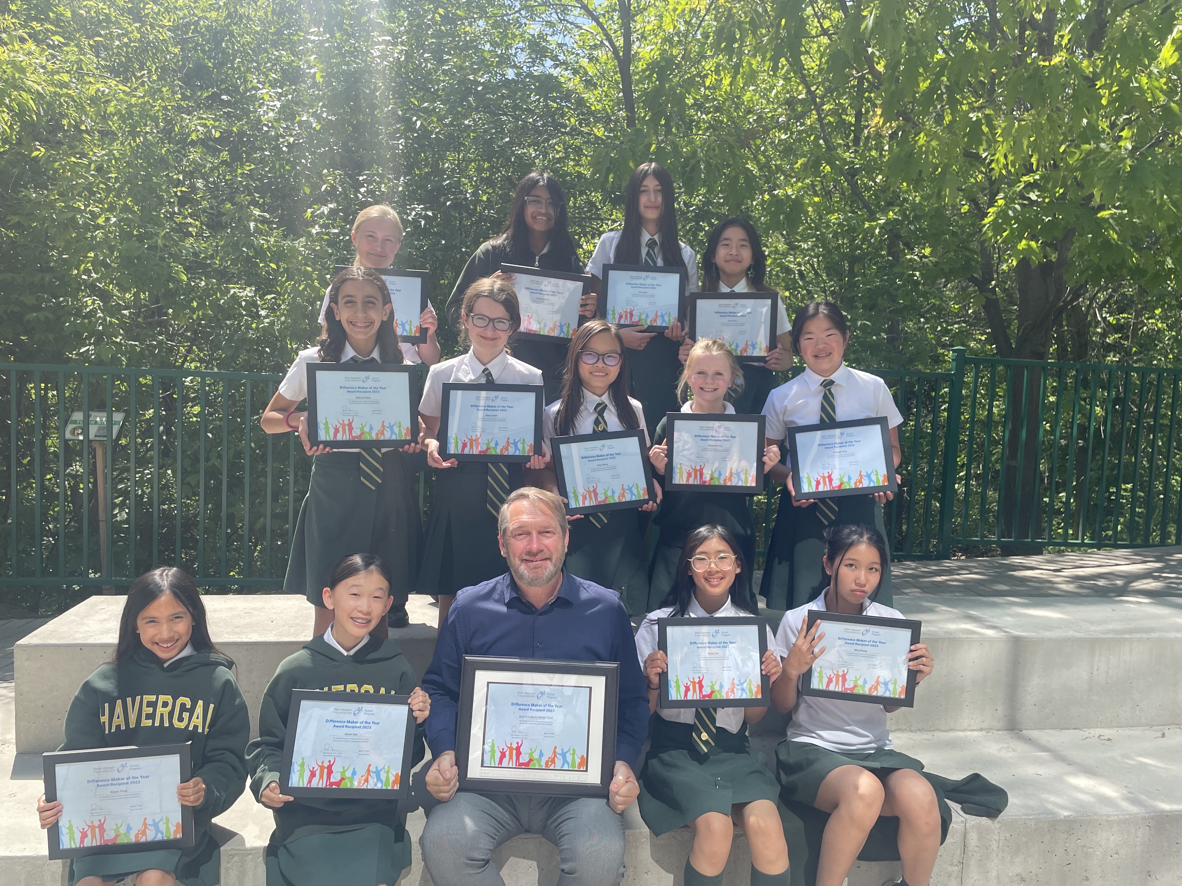 A group of young students and their teacher holding their Difference Maker of the Year Award certificates. They are outside.  