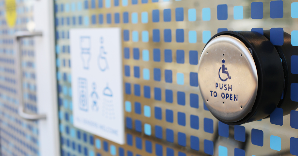 Accessible door button beside inclusive washroom signage