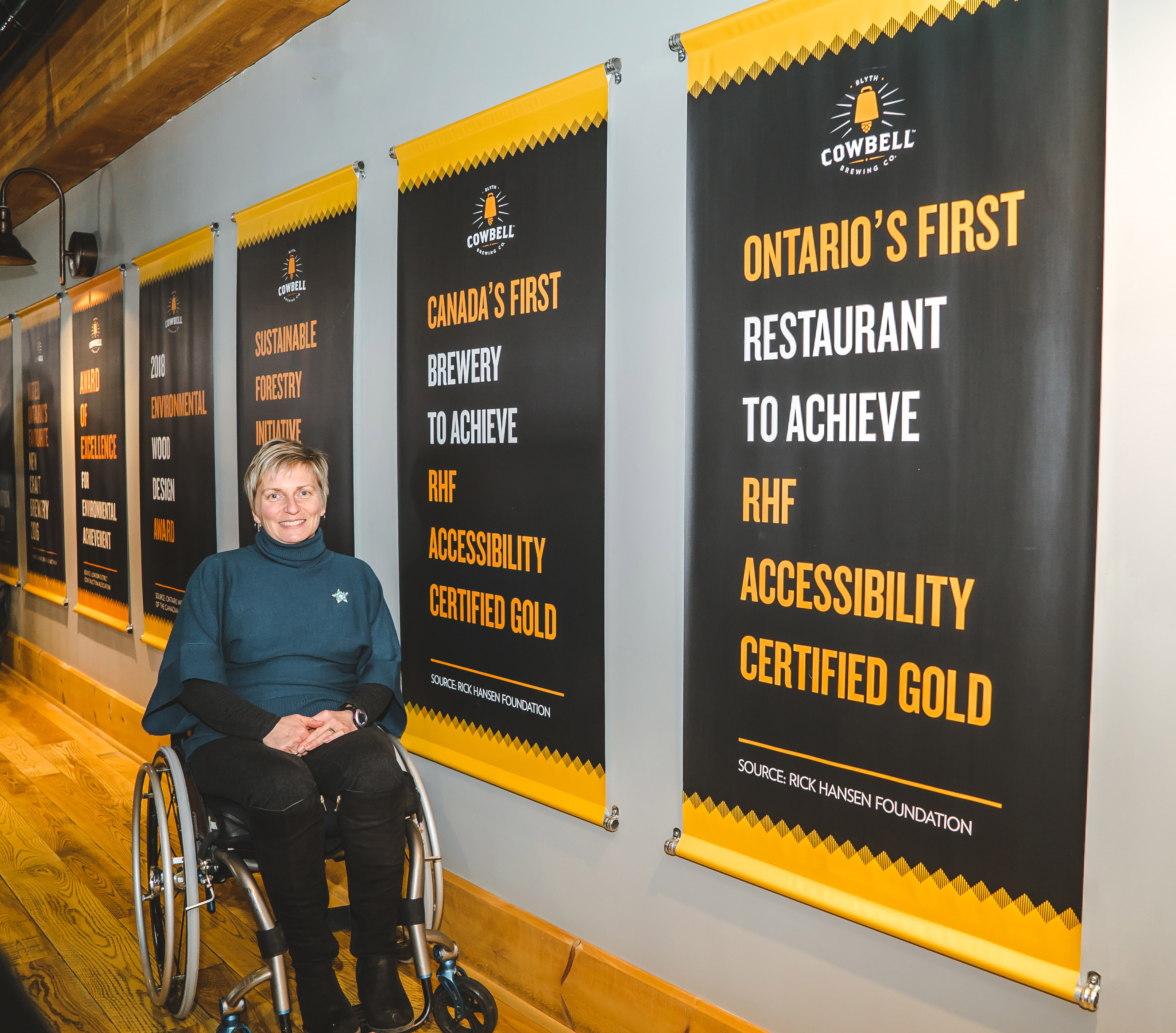 Julie, a woman using a wheelchair, smiles beside posters celebrating the Gold Accessibility Certification