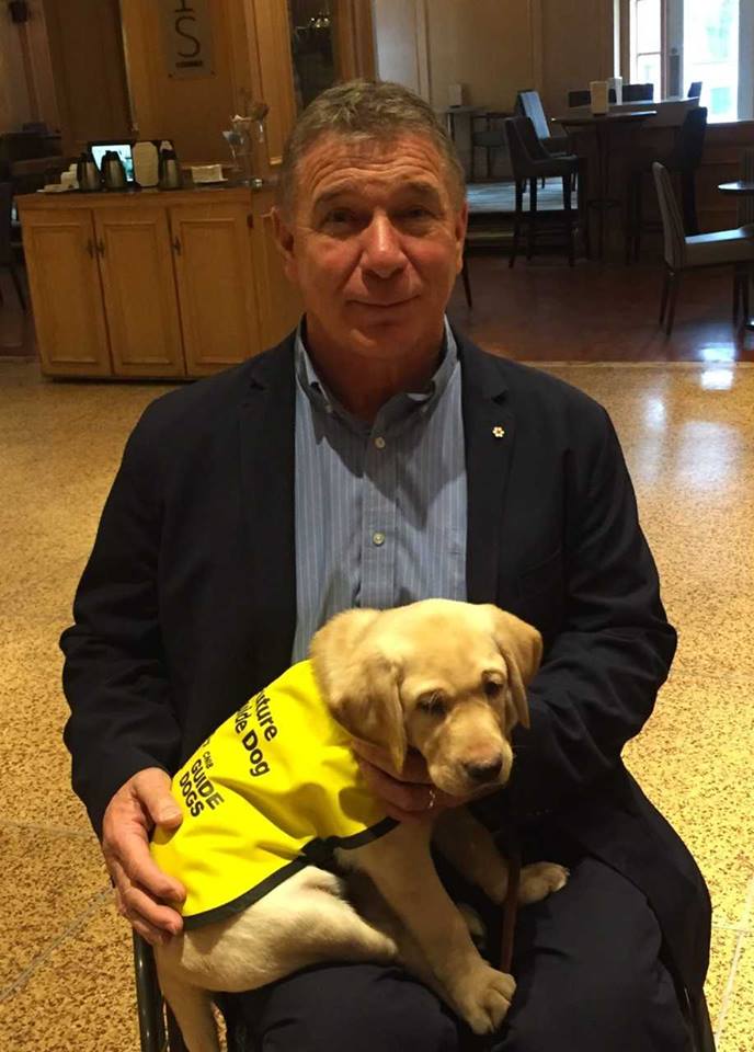 In a photograph from 2018, Rick Hansen holds a golden lab retriever puppy named Sherman. Sherman is now a working CNIB guide dog in Ontario!