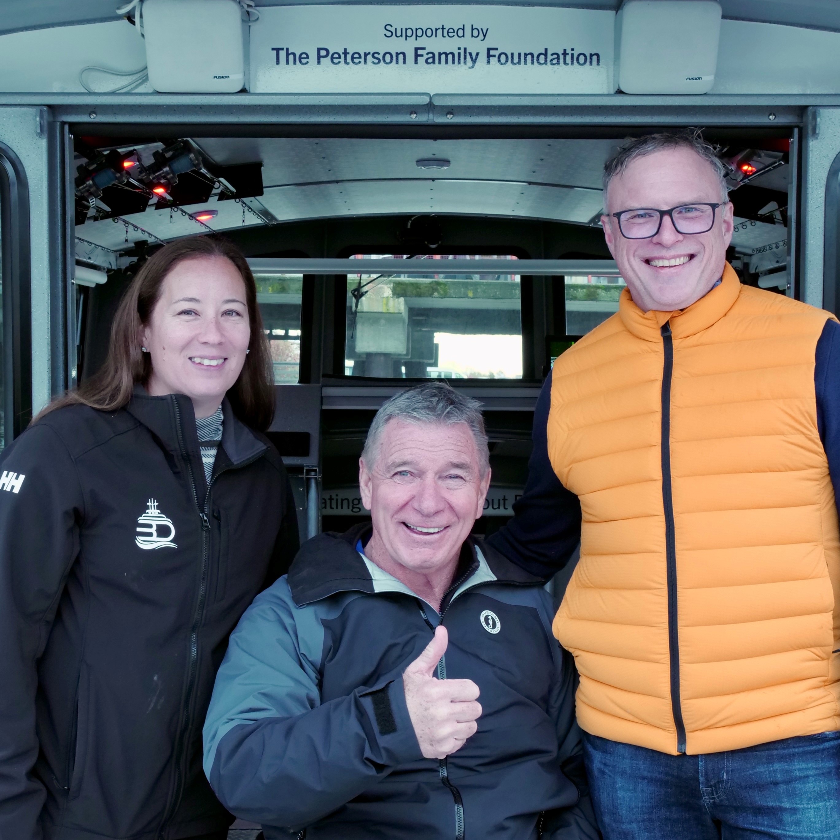 Ryan and Monica Peterson stand next to Rick Hansen beneath a plaque that reads 'supported by the Peterson Family Foundation'.