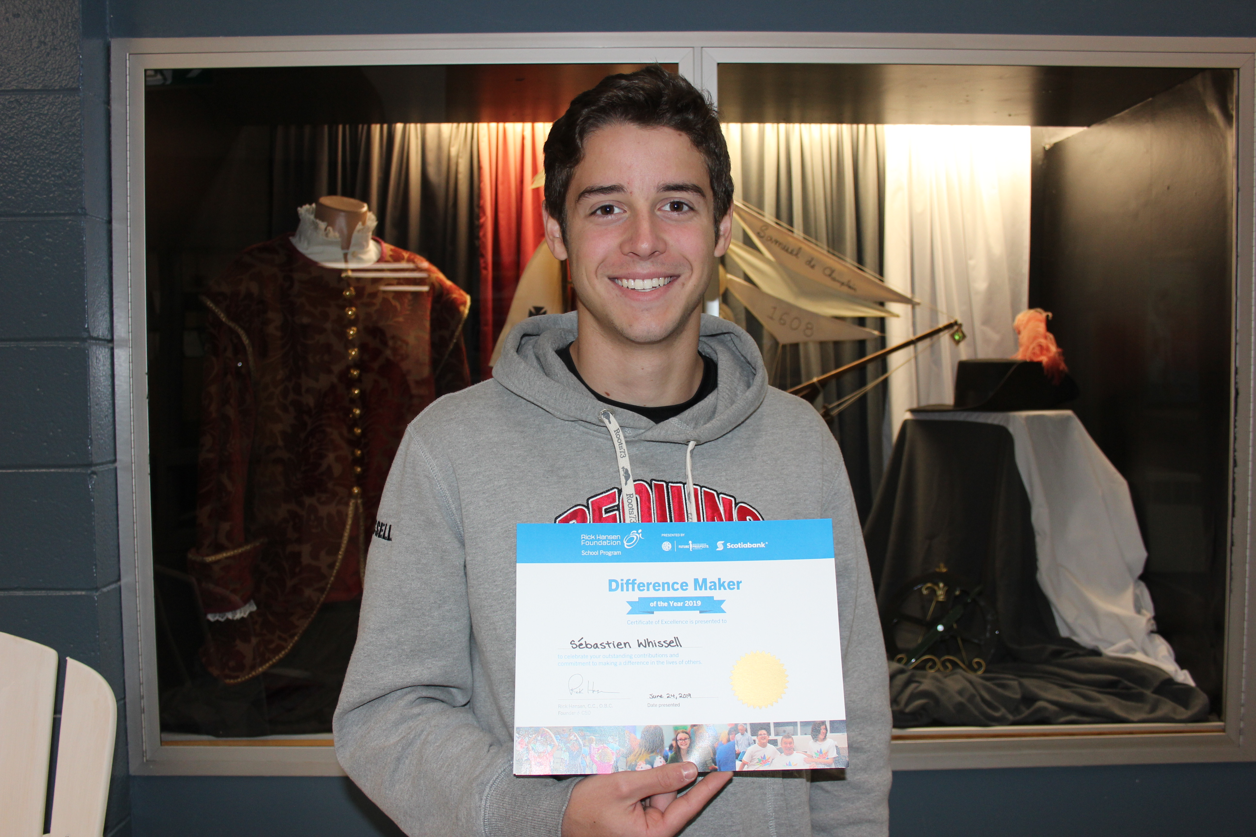 Young brown with brown hair, wearing sweater smiles holding up DM year certificate. 