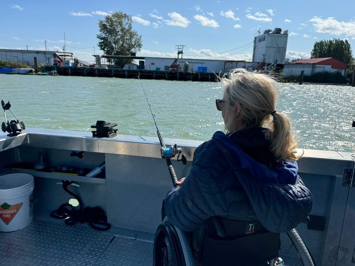 A woman in a wheelchair on a platform above the water, holding a fishing rod and looking at the water