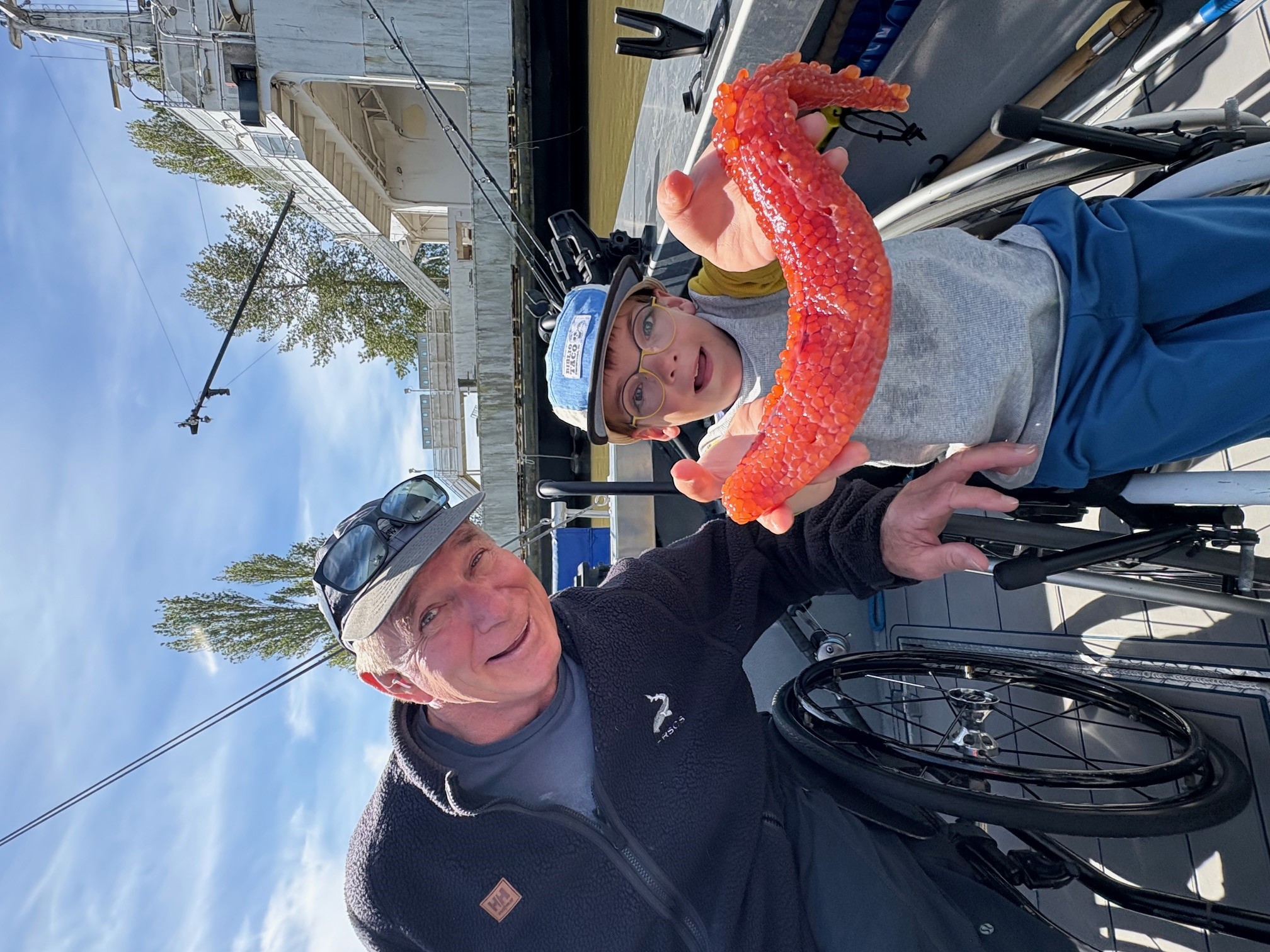 A person in a wheelchair on a boat showing a bright red sea creature while another person looks on.