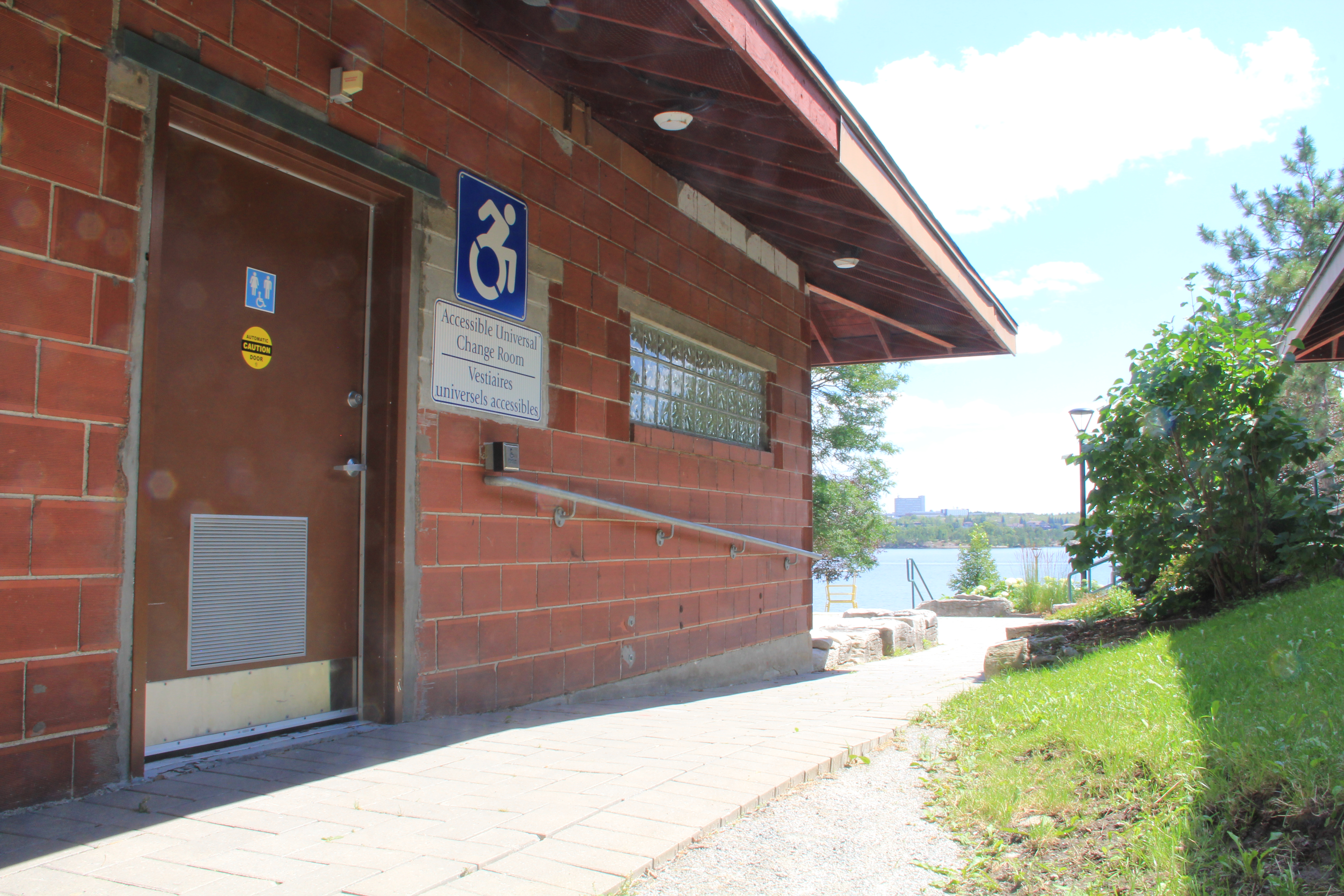 Brick building with accessible wheelchair ramp. There is a blue sign with a white wheelchair icon and a sign below it that reads accessible universal change room.