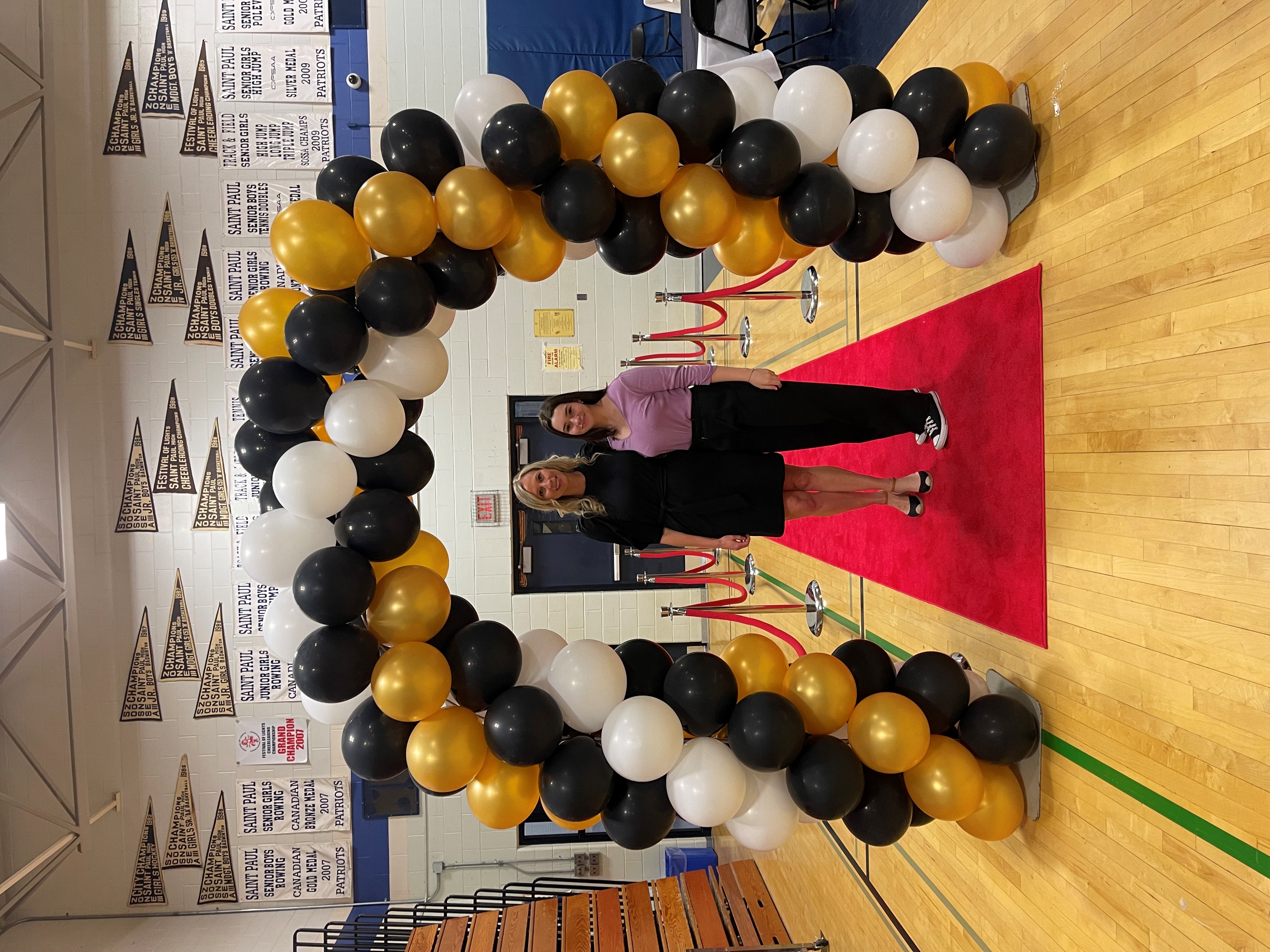 Mackenzie standing next to her teacher under a balloon arch at the Time to Shine prom.