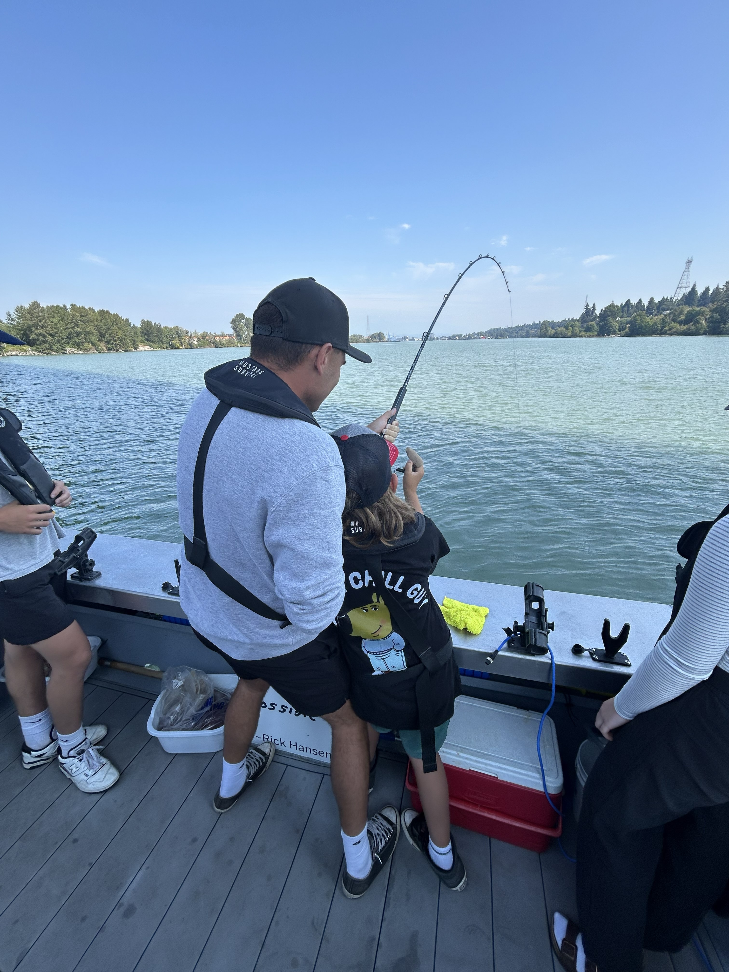 Adult and child standing together on a fishing boat, holding a fishing rod over the water while other passengers look on nearby.