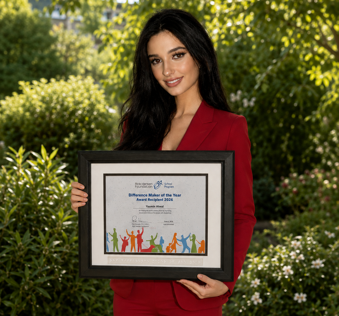 Young woman with long dark hair standing outdoors in front of greenery, wearing a red suit and holding a framed “Difference Maker of the Year Award Recipient 2026” certificate.