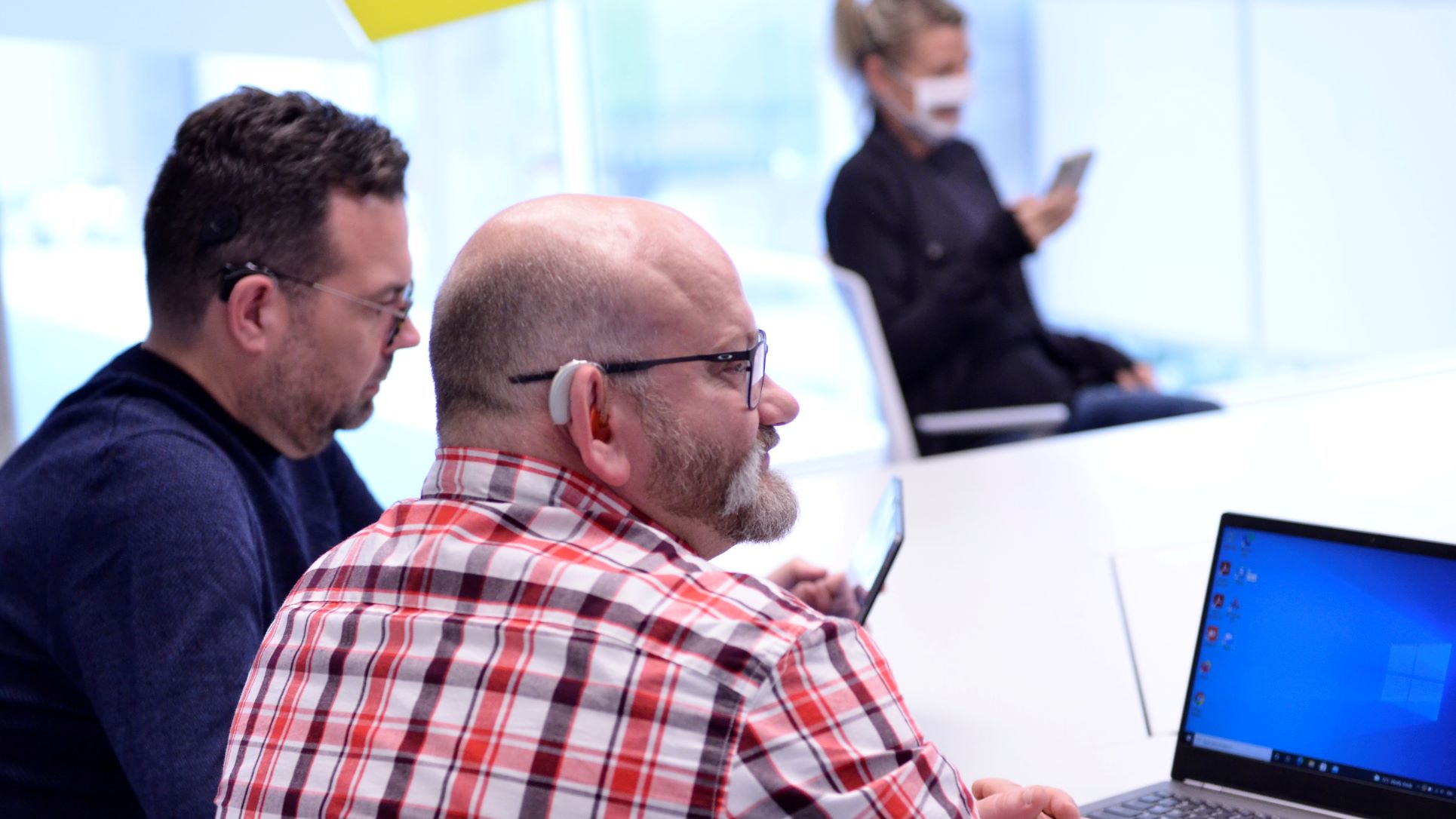 group of professionally dressed people, using laptop on phone, with hearing aids at board room table