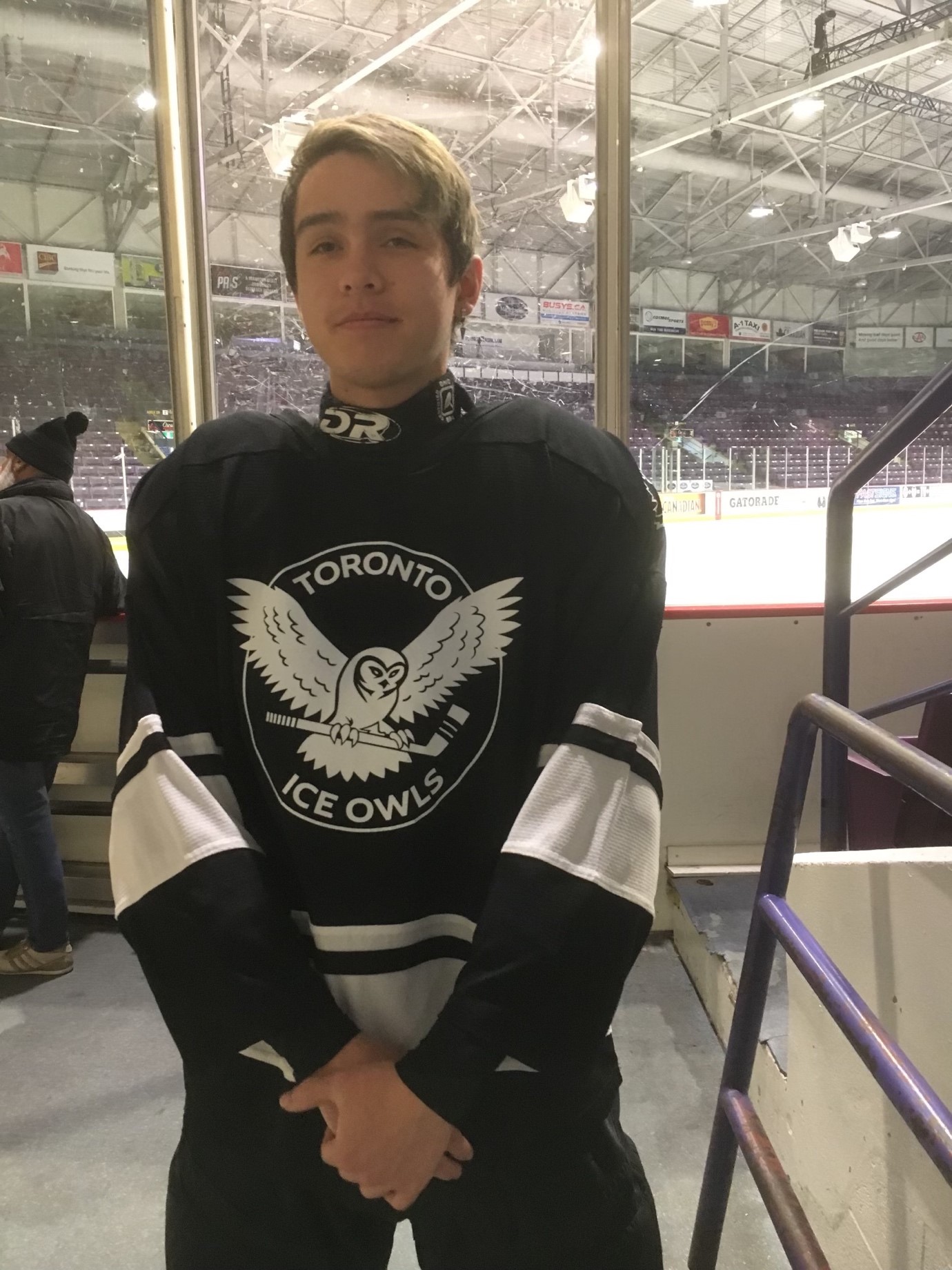 Young man wearing hockey equipment and posing in front of rink.