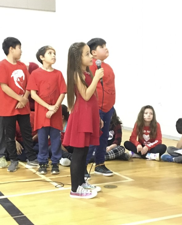 Young girl in red shirt speaks at assembly