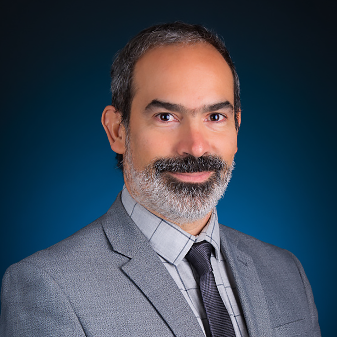 Portrait of a man with short salt and pepper hair wearing a grey suit with a grey checked shirt and black tie