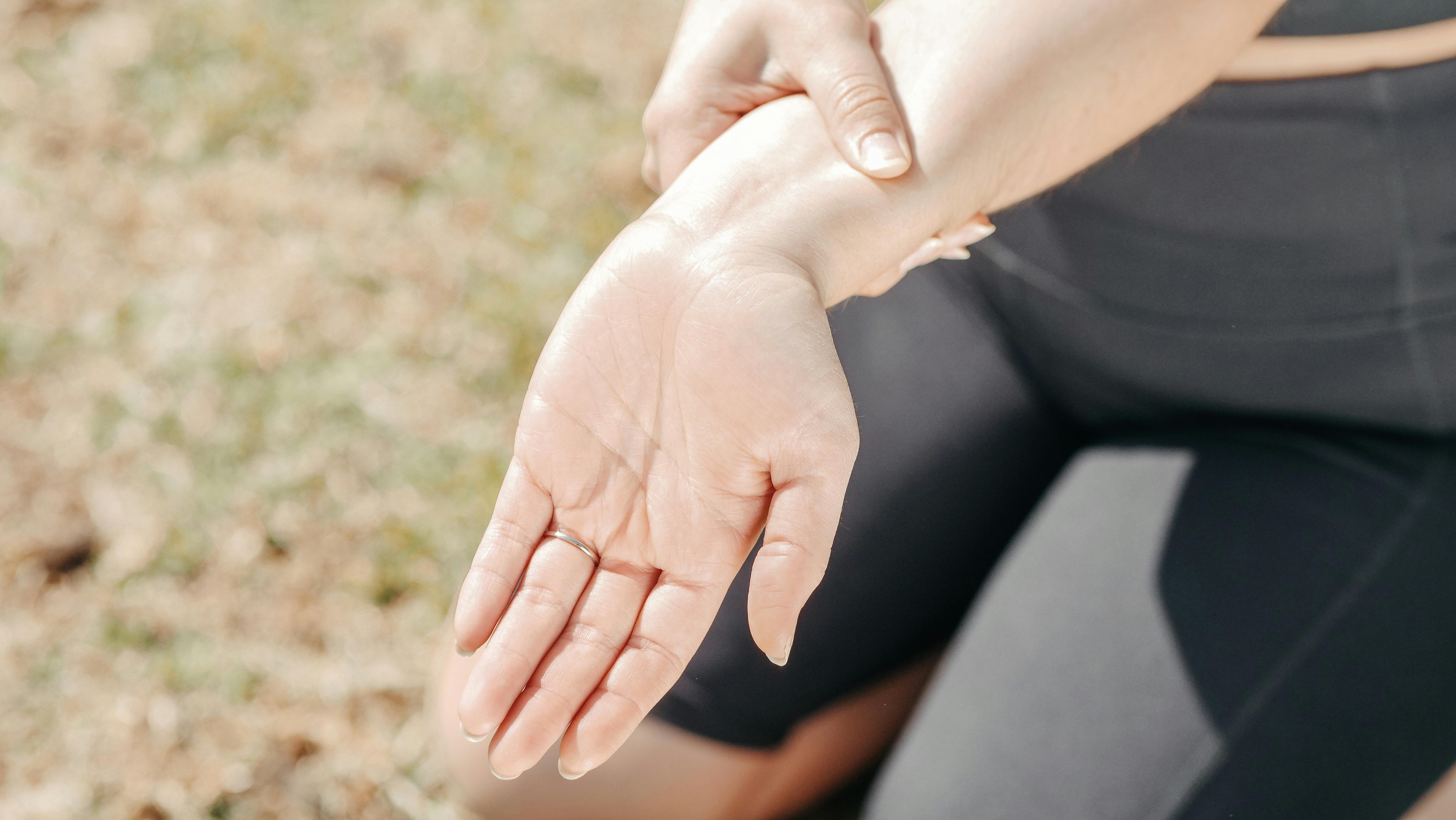 Close-up of a person outdoors holding their forearm with the opposite hand, palm facing upward