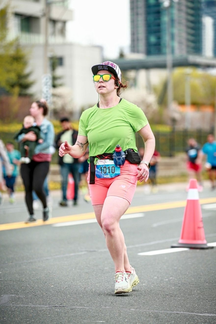 Rachel Ganz running the marathon. She is wearing sunglasses, a green shirt and bright orange shorts.