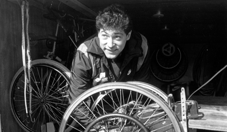 Don Alder in midst of fixing bike wheel looking at the camera. 