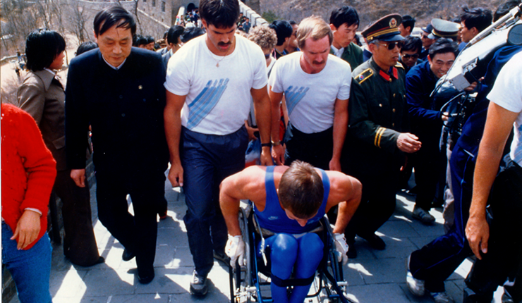 Rick Hansen accompanied by Mike Reid going through a crowd. 