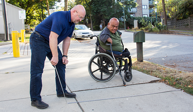 A RHF instructor teaches a man in a wheelchair instructions pointing to a metal stick. 