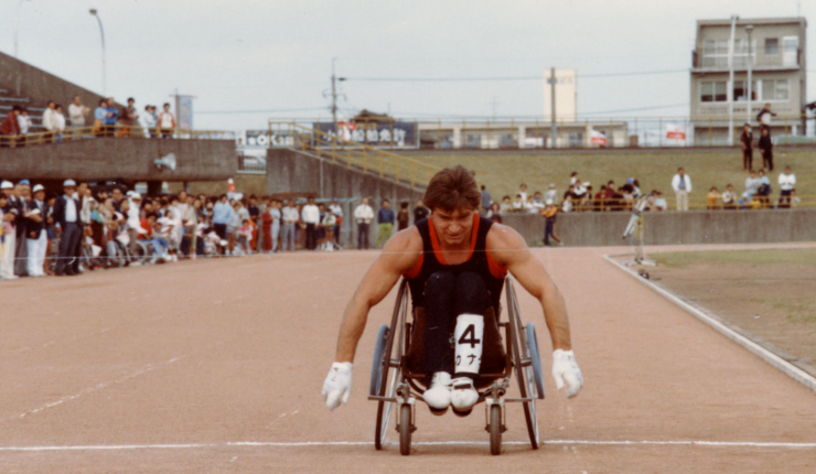 Rick Hansen cycling through the track field. 