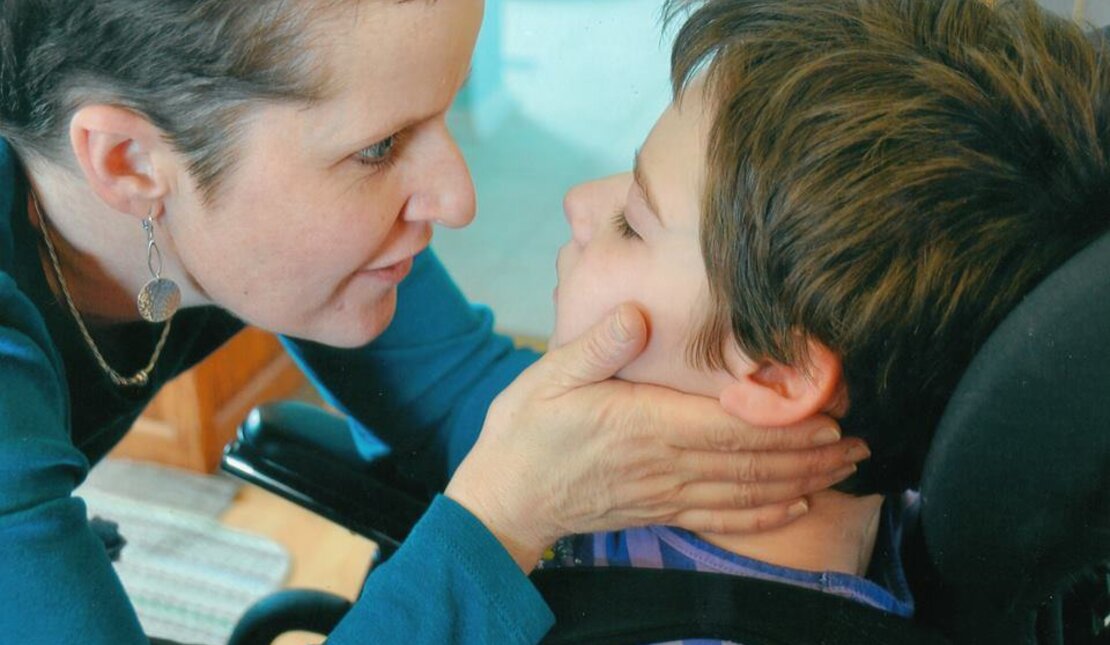 Woman gently holding onto the face of a girl in a wheelchair 