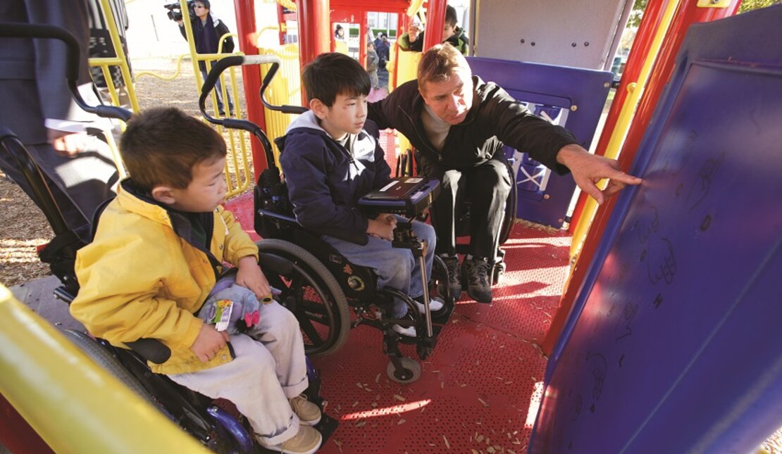 Rick and two young wheelchair users test out an accessible playground