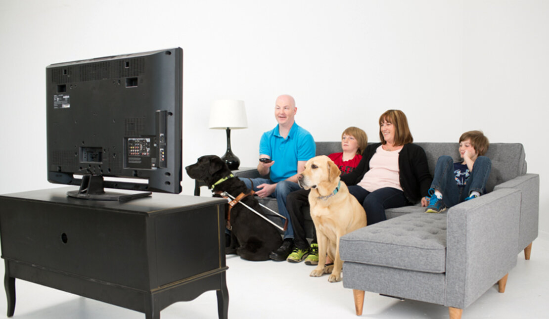 A family, and guide dog, watching television