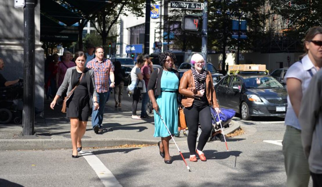 Two people with disabilities cross the street in downtown Vancouver