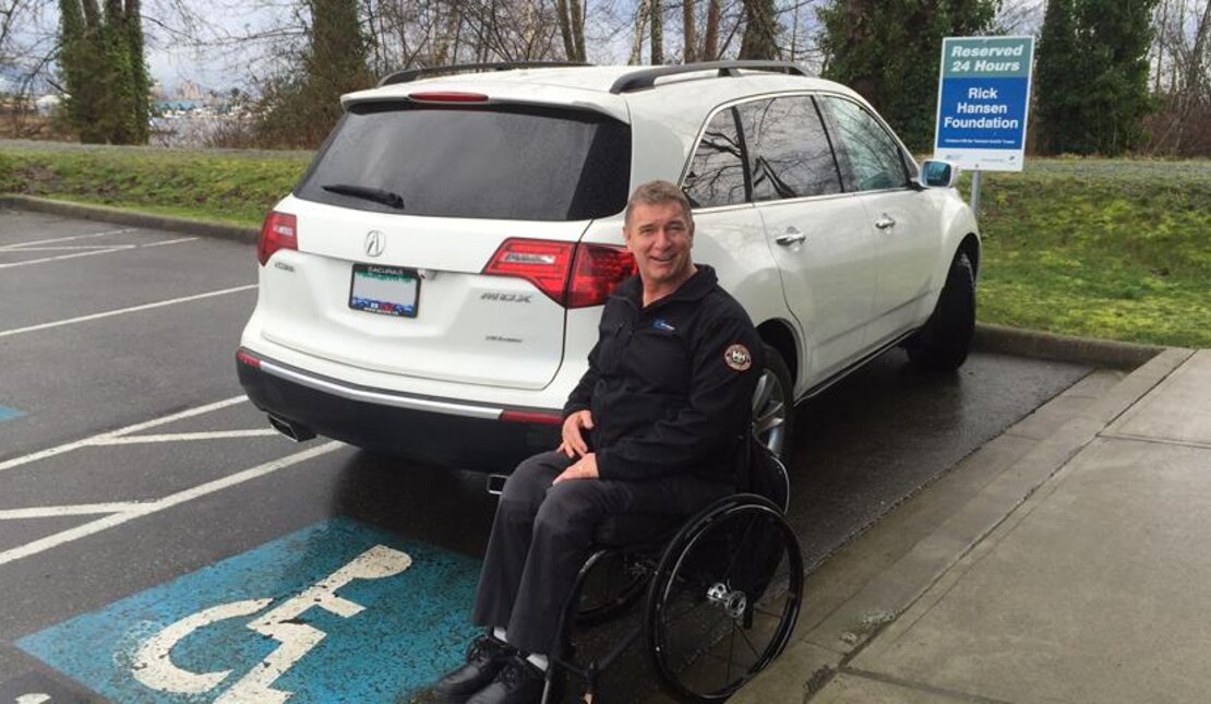 Rick Hansen by an accessible parking space outdoors