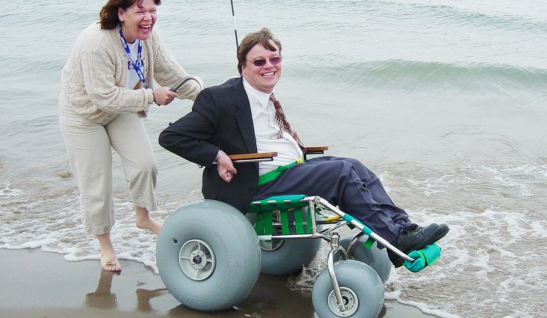 Happy woman pushing man in a beach wheelchair