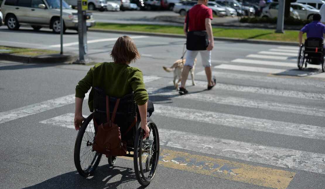 A woman uses a wheelchair while crossing a city street