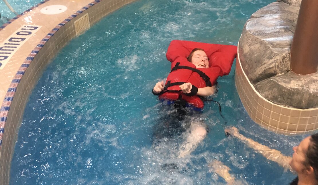 Eva at the pool,  floats in the lazy river wearing a life jacket 