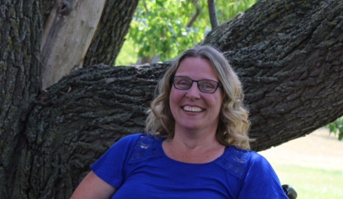 woman smiling sitting in wheelchair outside with a tree