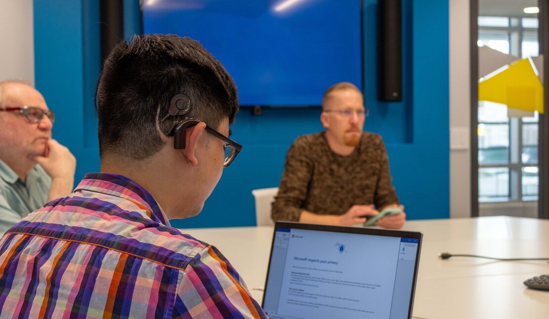 three men at a board room table, using hearing aids