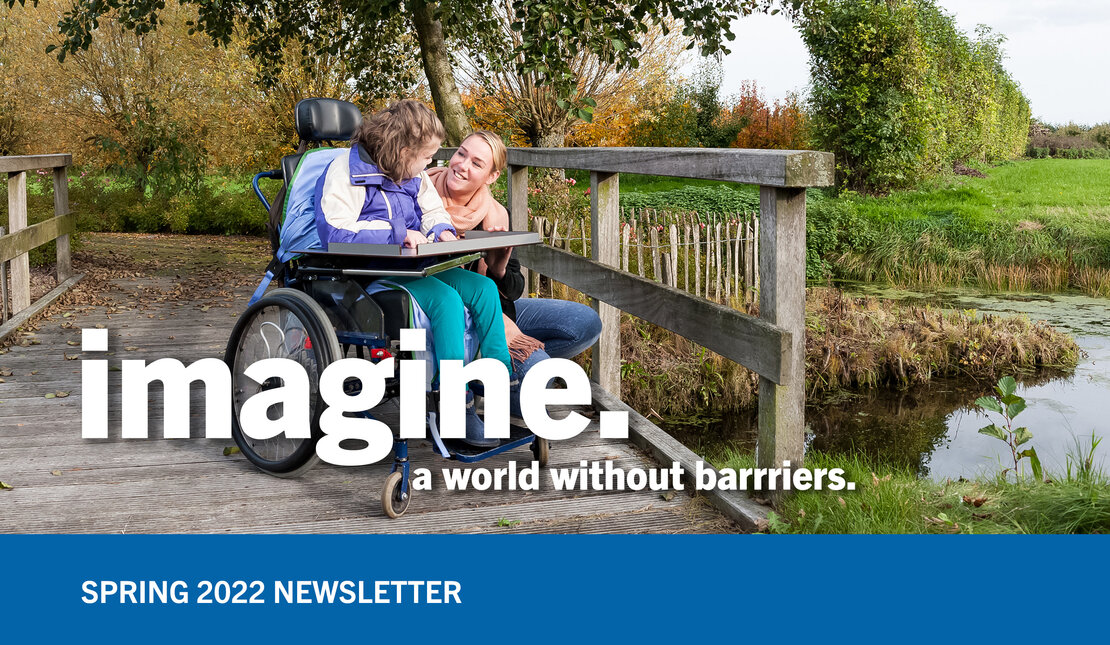 A girl in a wheelchair is looking at a woman kneeling beside her. They are on a wooden bridge. Imagine a world with our barriers is written in white. In a blue banner below, Spring 2022 Newsletter is written in white.