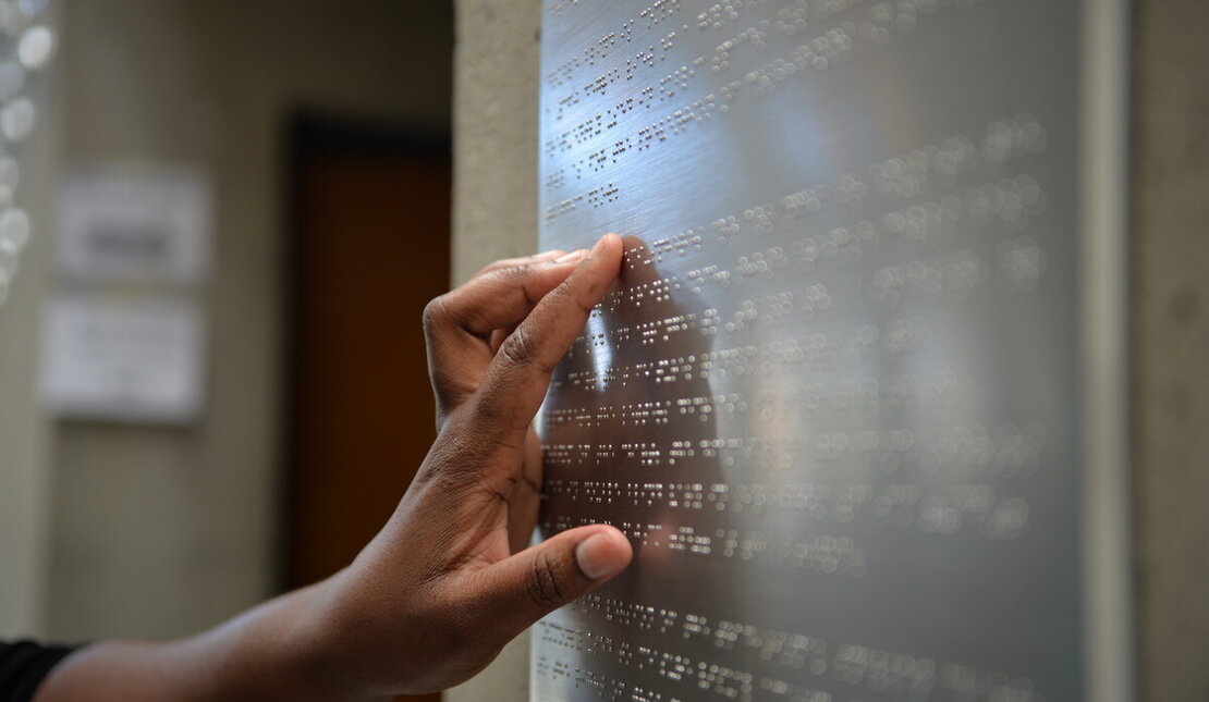 Hand of person reading braille on a metal sign. 