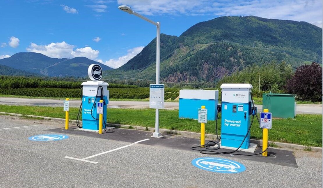 Accessible electric vehicle charging stations in Agassiz, British Columbia. The charging stations are blue and white. There are mountains in the background.