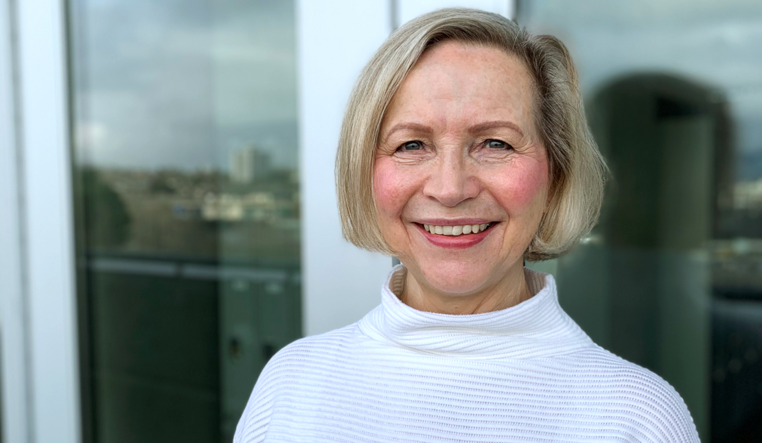 Pat Short wearing a white turtleneck sweater and smiling at the camera. Pat has chin-length light coloured hair.