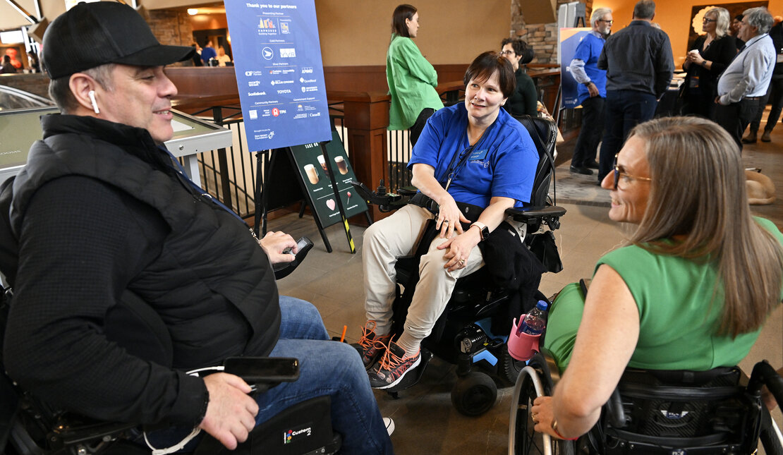 Three people who are using wheelchairs having a conversation at a conference. 