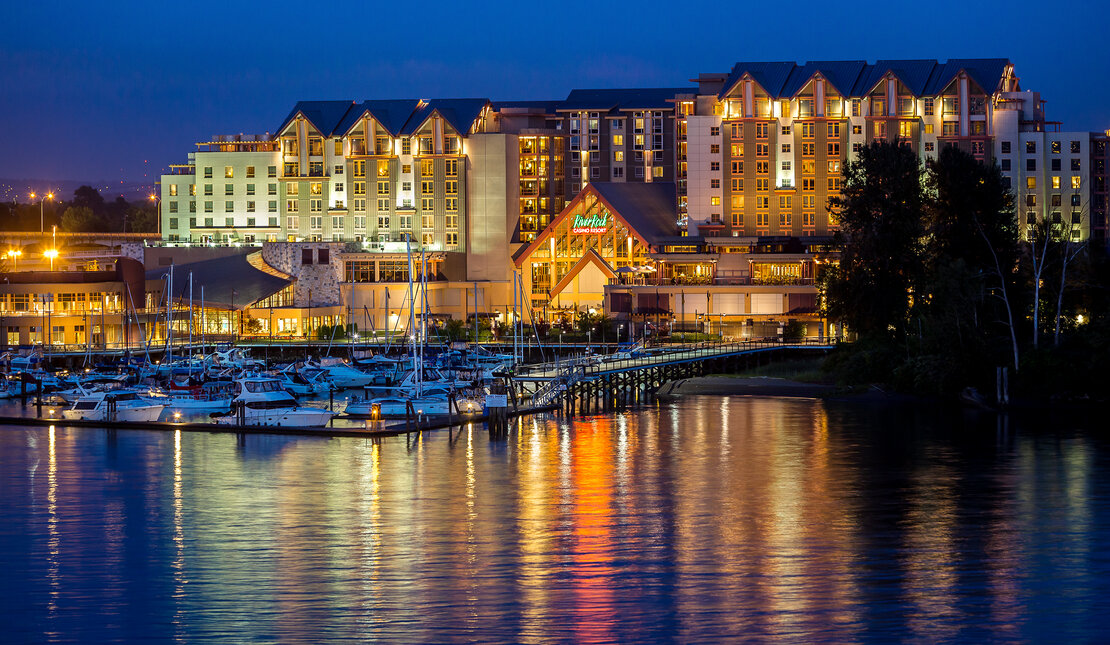 Building on the water lit up at night with boats in the foreground 