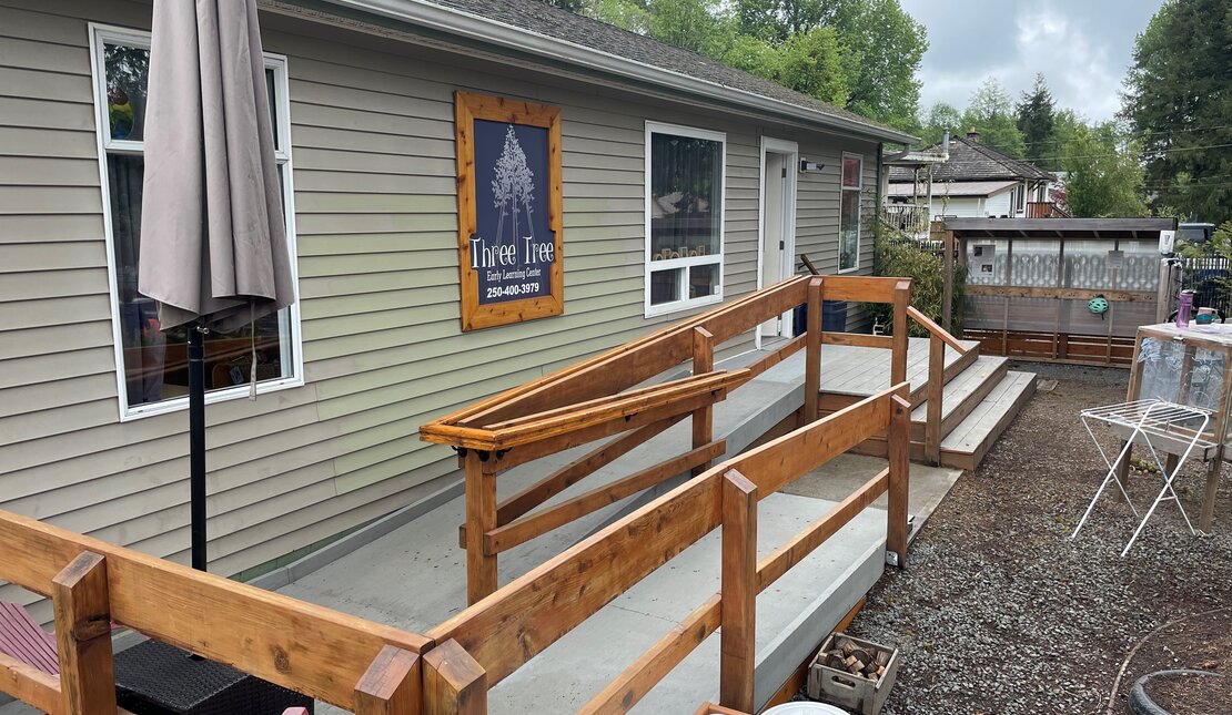 A long building with a dark blue sign that reads "Three Tree Early Learning Centre." There is a large accessible ramp attached to the building.