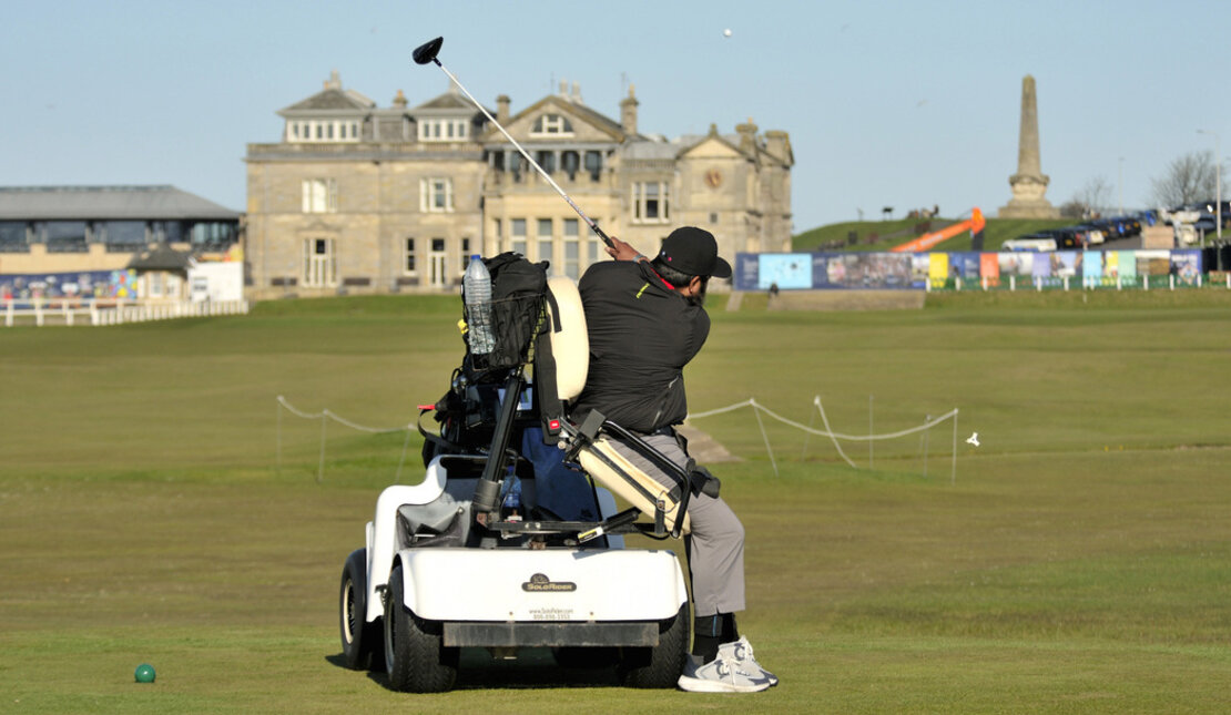 Man hitting golf ball while using adaptive golf cart on St. Andrews golf course.