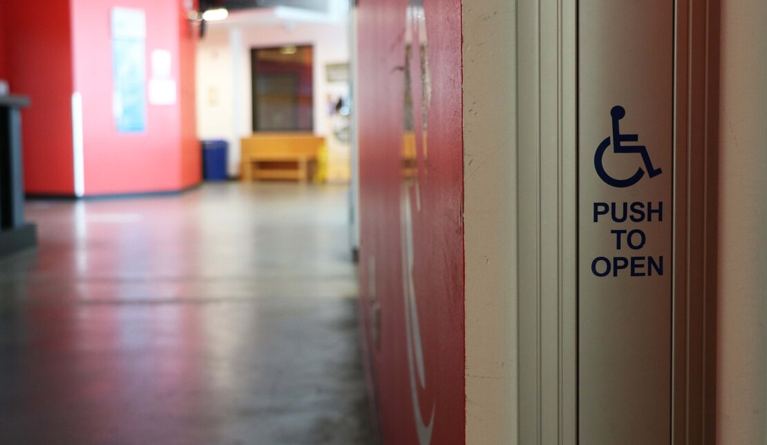 An accessible push to open button in front of a hallway. The walls of the hallway are red.