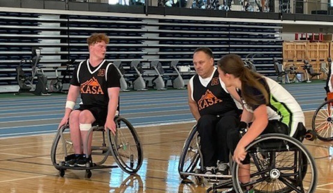 Cameron playing wheelchair basketball with two other players in a gym. 