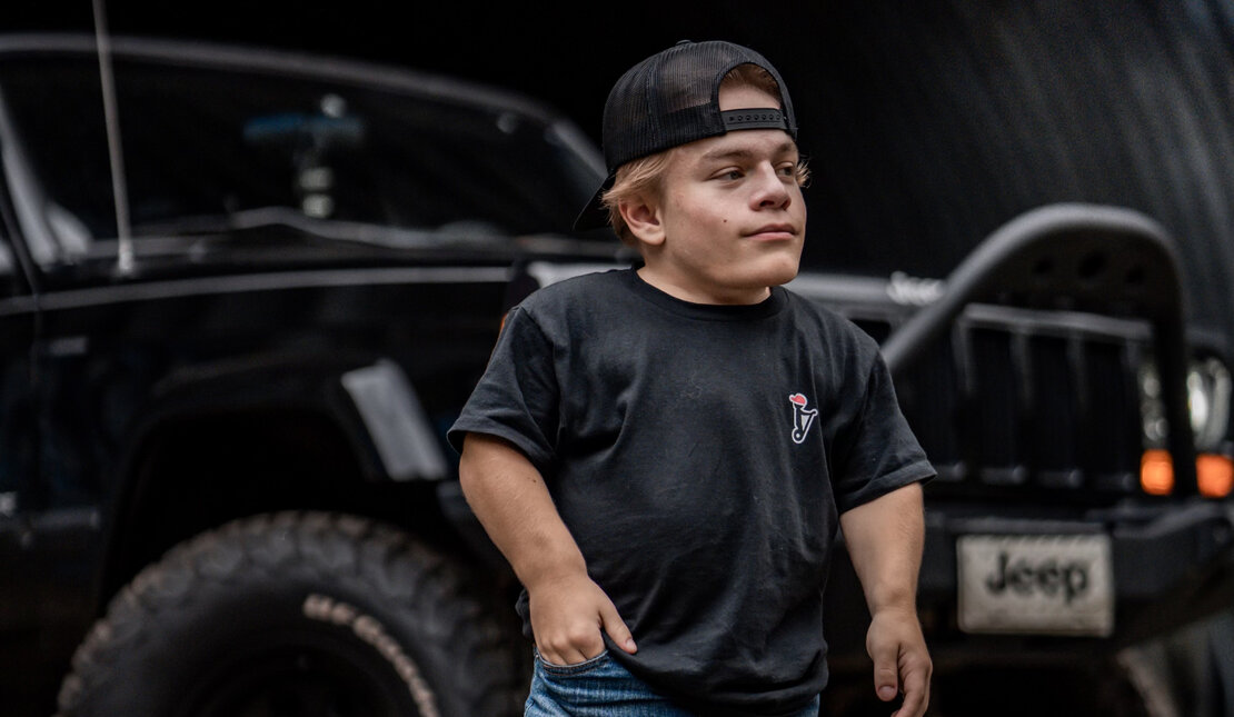Caden in a black shirt and jeans standing in front of his Jeep