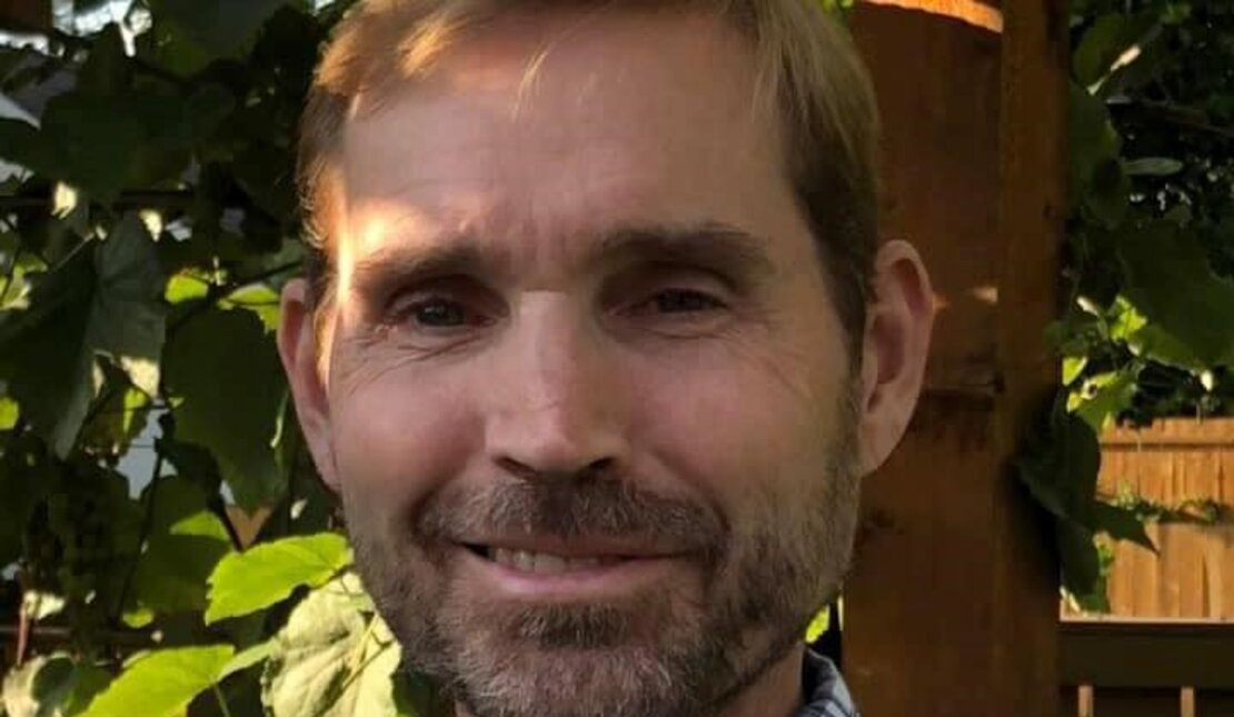 A headshot of Keith outside in front a tree. He is wearing a blue plaid shirt and has short brown hair.