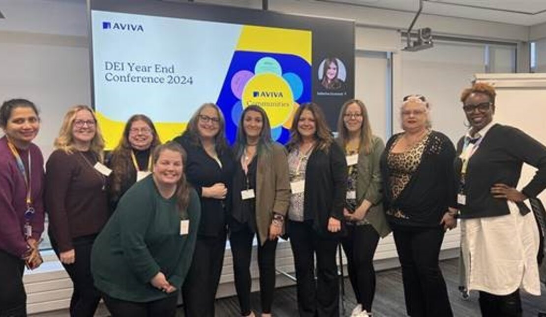 Ten women are standing in a conference room. Behind them, a projector screen displays the "Aviva" logo and "DEI Year End Conference 2024."