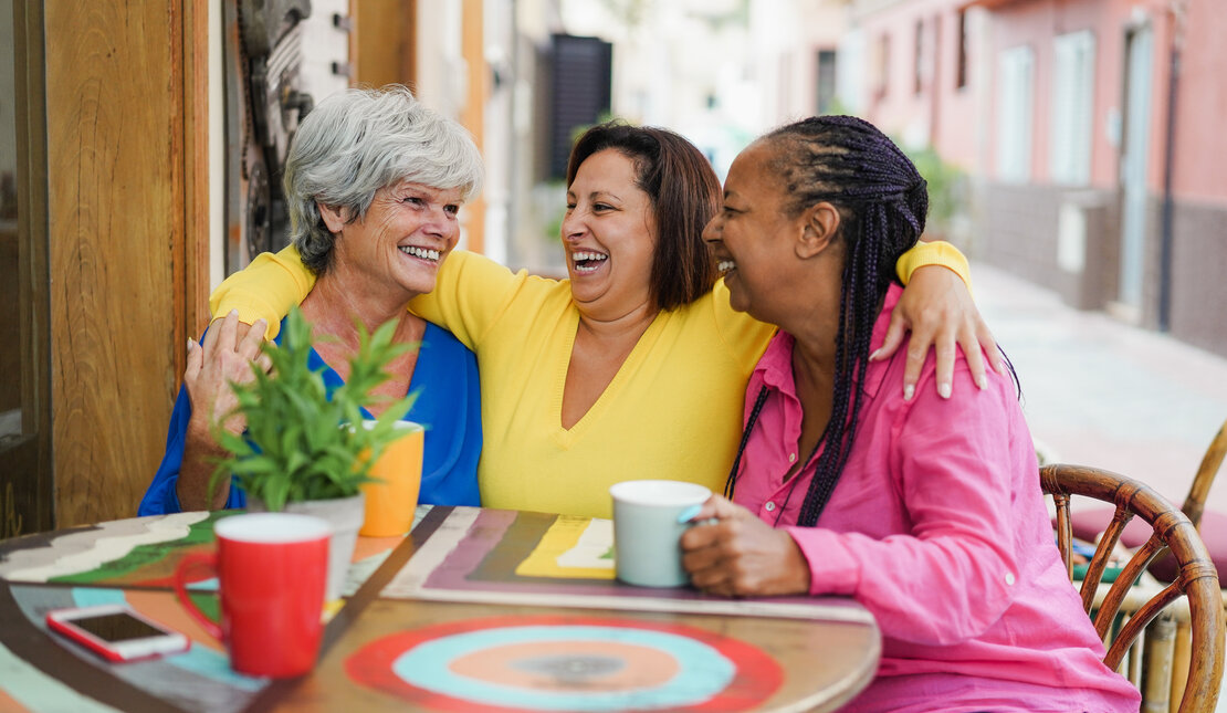 Three middle age woman standing  and holding a paper coffee cup. They are engaged in conversation