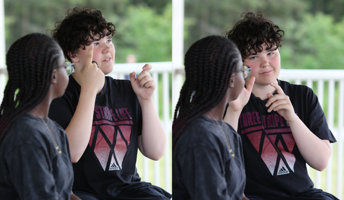 Two students sit outdoors facing each other and communicating using sign language